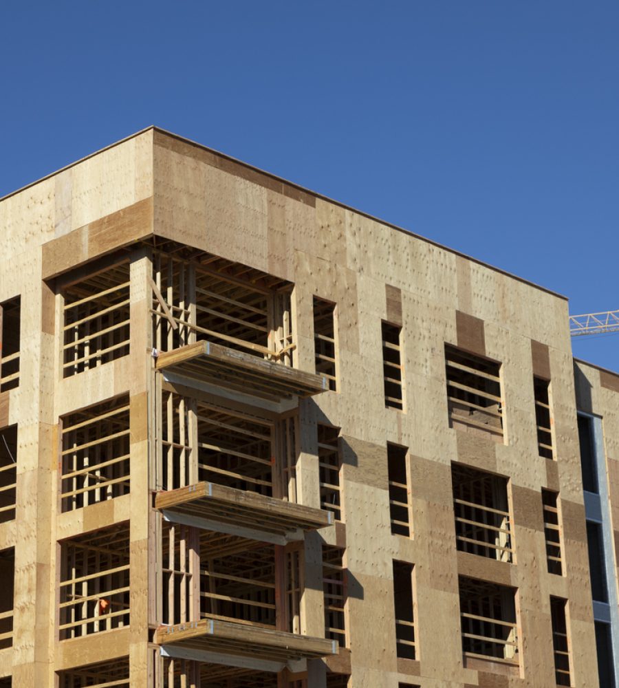 A construction site in Tallahassee, Florida, featuring a towering yellow crane above a multi-story residential complex in progress. The building, with exposed wooden framing and partially installed exterior cladding, represents the city's ongoing urban development and housing expansion.